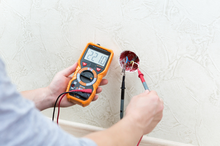 Close-up of man measuring and cheking power supply voltage with digital multimeterの写真素材