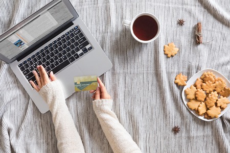 Top view of woman hands holding credit card on autumn baclground, business concept, online shopping, workspace with laptop, mobile phone, autumn leaves and flowers and notebook, cookies, flat lay.の写真素材