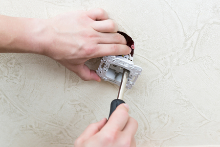 Male electrician puts on and repair an electrical outletの写真素材