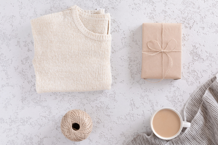 Brown kraft gift box, knitted sweater, jute rope and coffee cup on white textured table, top view and flat layの写真素材