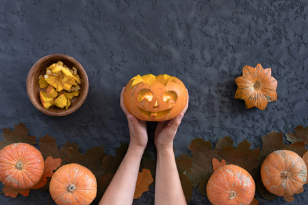 Halloween pumpkins over dark plaster background, top view, flat lay with copy space. Funny face jack-o-lantern carved in a pumpkinの写真素材