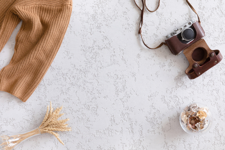 Hello Autumn flat lay background. Top view of workspace or office desk with vintage photo camera, sweater, autumn flowers and gold ears of wheat on textured white backgroundの写真素材