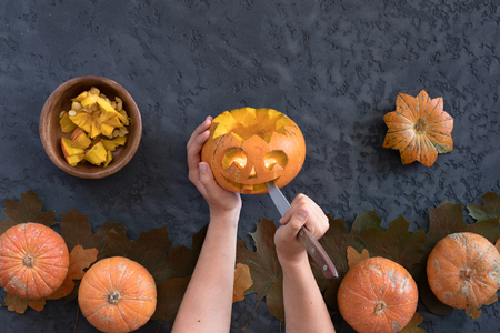 Top view of woman carves face of a jack-o'-lantern on orange halloween pumpkin, flat lay on black backgroundの写真素材