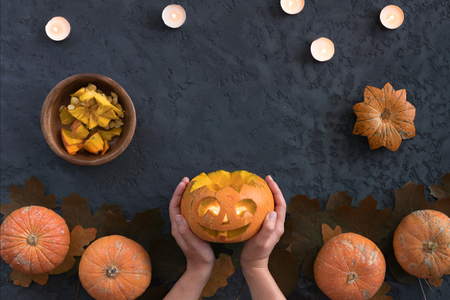 Top view of woman carves face of a jack-o'-lantern on orange halloween pumpkin, flat lay on black backgroundの写真素材