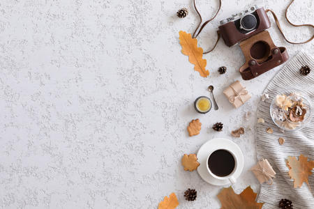 Hello Autumn flat lay background. Top view of workspace or office desk with vintage photo camera, sweater, cup of coffee, honey cookies, flowers and gold ears of wheat on textured white backgroundの写真素材