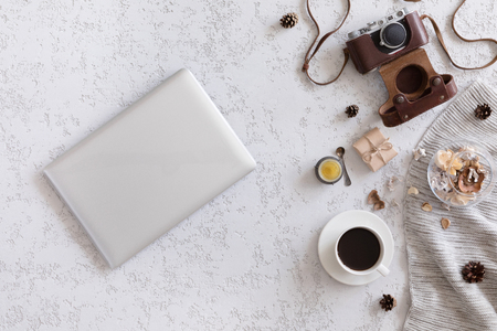 Winter flat lay background. Top view of workspace or office desk with laptop, vintage photo camera, blanket, cup of coffee, ginger cookies, cone on textured white backgroundの写真素材