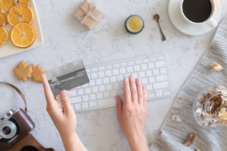 Top view of woman hands holding credit card on autumn baclground, business concept, online shopping, workspace with laptop, mobile phone, autumn leaves and flowers and notebook, cookies, flat lay.の写真素材