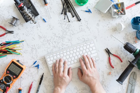 Top view of different electrical tools on white concrete background, man hand on computer keyboard, flat lay. Tools for an electrician, voltages and current measurementsの写真素材