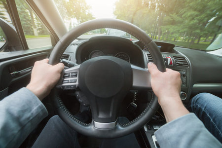 Travel by car background. Close-up of man's hand on steering wheel, driving a car at sunset.