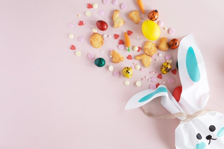 Top view and flat lay of Easter painted eggs, cookies, sprinkles and candies arranged on pink background. Bunny Bag or basket with sweet giftsの写真素材