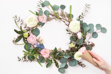 Festive flower wreath composition with kraft paper cornet and woman hand on white background. Overhead view, flat layの写真素材