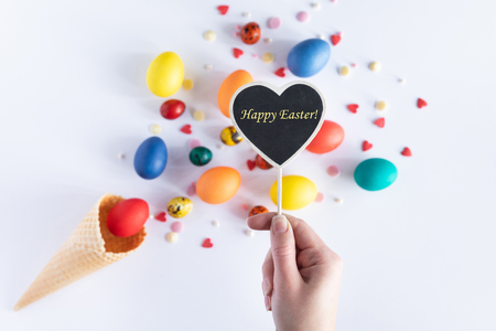 Top view of heart shaped sign with space for an inscription. Happy Easter greeting card. Arrangement with colorful easter eggs in waffle cone with place for text, isolated on white background, flatlayの写真素材