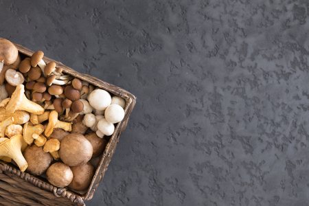 View from above of wicker basket with forest rare delicious edible mushrooms on a dark textural background, flat lay.の写真素材
