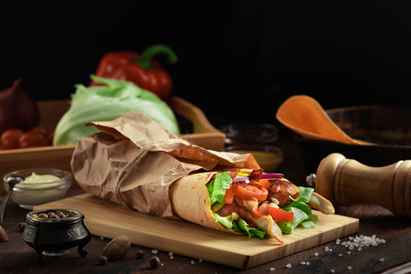 Mexican burrito wrap with corn tortilla, chicken meat and vegetables on dark rustic background. Chicken grilled shawarma with bacon, pita bread, tomatos and salad and different sauces.の写真素材