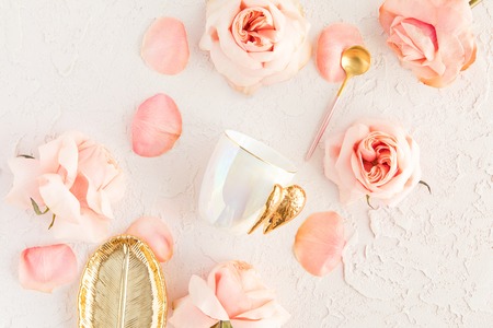 Stylish coffee or tea set on pastel background with pink flowers, leaf golden plate and spoon with roses and petals. Flatlay, top view on pastel concrete backgroundの写真素材