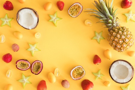 Exotic tropical fruit background. Colorful fresh exotic fruits on pastel yellow table. Pineapple, coconut, passion fruit, strawberry, carambola, lychee, kumquat. Flat lay, top view, copy spaceの写真素材
