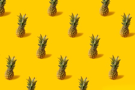 Summer colorful fruit minimal pattern of fresh pineapples on yellow background with shadowの写真素材