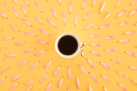 Top view of white cup of tea ot coffee on yellow table with pink petals. Summer creative background and flatlayの写真素材