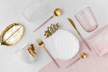 Flat lay of table decor. Top view of decorations for a serving festive table. White and golden pineapple plate, water glasses and pink cutlery on white background, flatlay.の写真素材