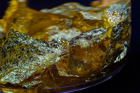 A little glass bottle with a wooden cork on a black surface with 22 Carat gold leaves macro close up