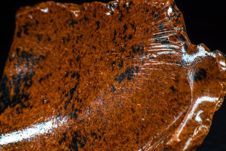 Real shiny specimen of orange Mahogany Obsidian volcanic stone macro isolated on black leather...