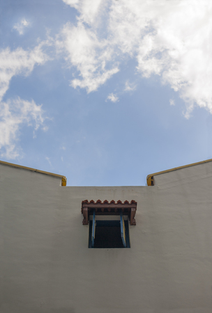 One blue window with some floating clouds. Cropped view of one window on an old shophouse during a...