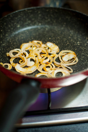 Close-up shot of some cut onions slowly getting caramelized in a frying pan in a kitchenの写真素材
