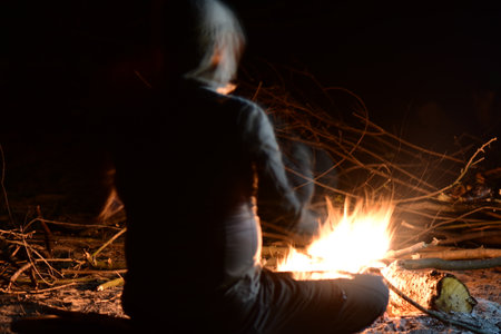 Man sitting near the bonfire in the forest at night. Selective focusの写真素材