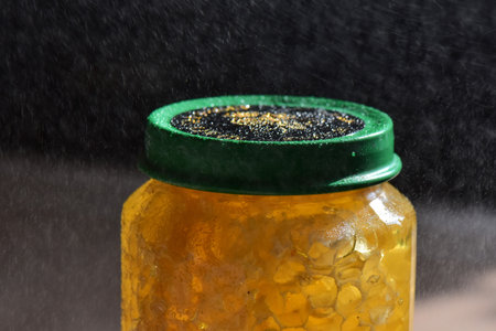 Honey in a glass jar with drops of water on a black background
