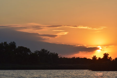 Beautiful sunset on the river with clouds and trees in the foregroundの写真素材