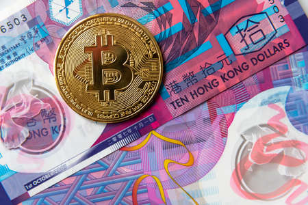 Golden Bitcoin Cryptocurrency coin on Hong Kong Dollar banknotes.の写真素材
