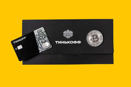 Moscow, Rissia - March 31, 2021: Black Metal Tinkoff Bank debit card and corporate black envelope (text translation from russian: Tinkoff) with silver bitcoin. Russian commercial bank founded by Oleg Tinkov.のeditorial素材
