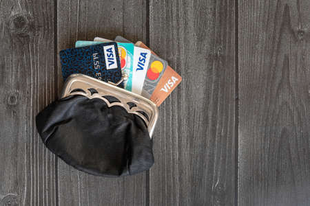 Moscow, Russia, January 17,2021 - Few credit cards (Visa, Mastercard and Mir) in the leather vintage wallet coin-box at wooden table, product concept shot.のeditorial素材