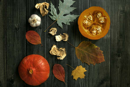 Autumn background with dried mushrooms, garlic and pumpkin. Dry tree leaves. Natural wooden background. Flat lay, top view.の写真素材