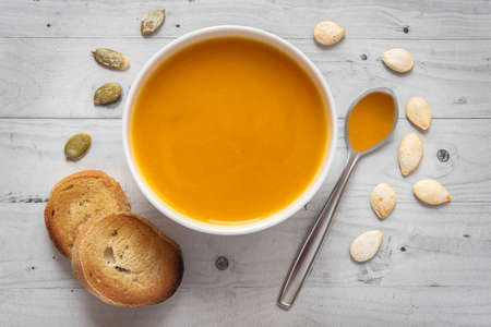 Pumpkin soup with bread on a light wooden background with spoon and seedsの写真素材