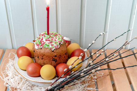 Ceramic plate with Easter cake, lit candle and painted eggs on a wooden table with willow branchesの写真素材