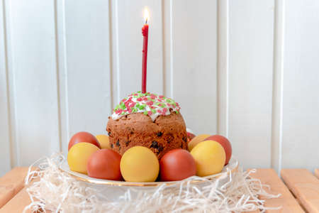 Ceramic plate with Easter cake, lit candle and painted eggs on a wooden table with willow branchesの写真素材