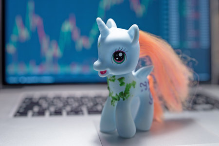 Unicorn toy on laptop on stock market graph background