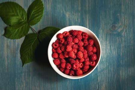 Fresh raspberries in bowl on blue wood table. Top view.の写真素材