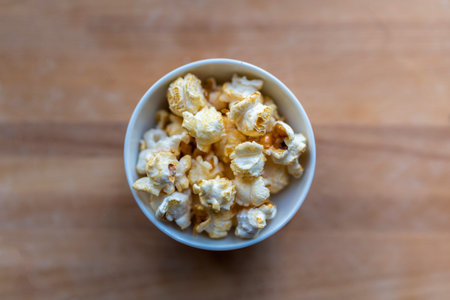 Popcorn with caramel in ceramic bowl on a wooden background. Top view, flat lay, copy space.