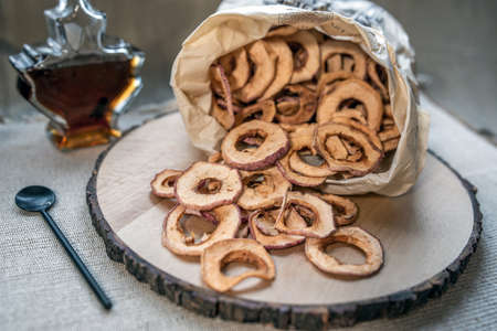 Dried apples spilled out of a paper bag on to a wooden table. An image with selective focusing.の写真素材