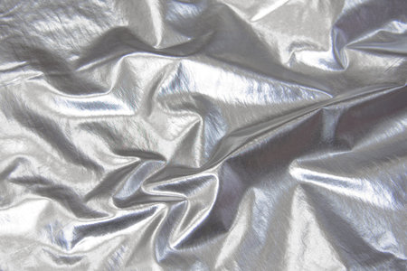 Wrinkled silver metallic fabric. Folded fabric which looks like foil. Metallic cloth. Light silver metallic. Warped crumpled fabric. Glossy cloth textureの写真素材