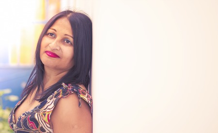 Pretty middle aged asian woman leaning against a white wall looking content.の写真素材