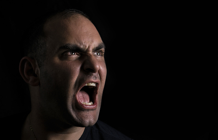 Headshot of an angry screaming man on in the darkness.の写真素材