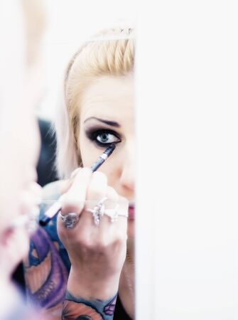 Woman with tattoos putting on make up in the mirrorの写真素材