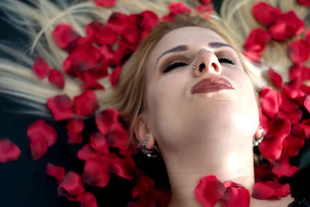 Pretty blonde woman relaxing with petals in her hairの写真素材