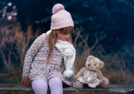 Little girl sitting on a bench with a teddy bearの写真素材
