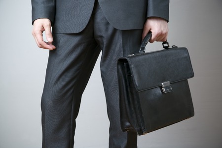 Businessman with briefcase in hand on gray backgroundの写真素材