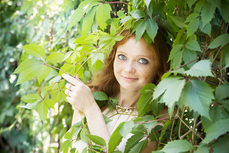 Portrait of redhead girl with blue eyes on nature. Face of young woman with freckles closeupの写真素材
