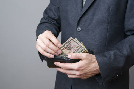 Businessman with money in purse in hands on a gray backgroundの写真素材
